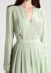 Mintgrünes Kleid mit einem geknöpften V-Ausschnitt, langen Ärmeln, gefälteltem Oberteil und einem strukturierten Taillenbund mit Zopfdetail.