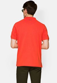 Czerwona koszulka polo z krótkim rękawem, z klasycznym kołnierzykiem, z prążkowanymi mankietami i logo marki nadrukowanym na tylnej części dekoltu.
