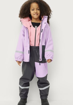 Purple waterproof jacket with a pink inner lining and gray pants, featuring reflective stripes and a large front pocket. Black footwear visible.