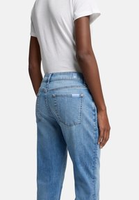 Ljusblå denimjeans med avslappnad passform, med två bakfickor och en subtil logotyp på midjebandet och fickan.