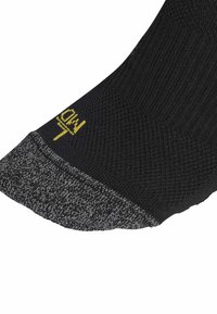 Calcetín negro con un cuerpo texturizado, puño gris con patrón y logo amarillo en el costado. Presenta un acabado suave y un diseño elástico.