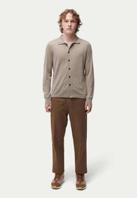 Beige knapplång cardigan med krage, kombinerad med bruna byxor och bruna och tan sneakers. Slät textur, figurnära design.