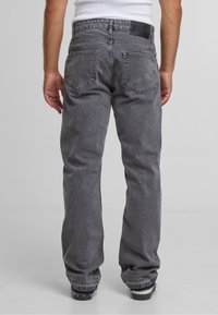 Jean en denim gris à coupe droite, avec des poches arrière cousues et une texture légèrement délavée. La taille est ornée d'une étiquette noire.