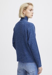 Sinine ribaga sviiter kõrge kraega, pikkade varrukatega ja tekstuurse viimistlusega. Kombineeritud helesiniste denim teksadega.