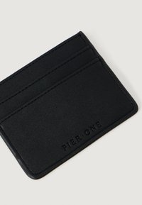 Melnā ādas karšu turētājs ar vairākiem vertikāliem slotiem, gluda tekstūra un iegriezta apzīmējuma "PIER ONE" virspusē.