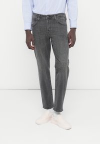 Γκρι τζιν παντελόνι με ευθεία κοπή, με ξεθωριασμένη υφή, παραδοσιακές τσέπες και διακριτικό πλύσιμο, σε συνδυα σμό με ανοιχτόχρωμα παπούτσια slip-on.