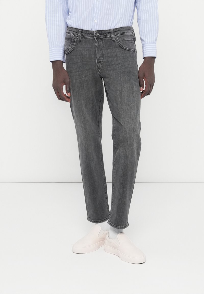 Γκρι τζιν παντελόνι με ευθεία κοπή, με ξεθωριασμένη υφή, παραδοσιακές τσέπες και διακριτικό πλύσιμο, σε συνδυασμό με ανοιχτόχρωμα παπούτσια slip-on.