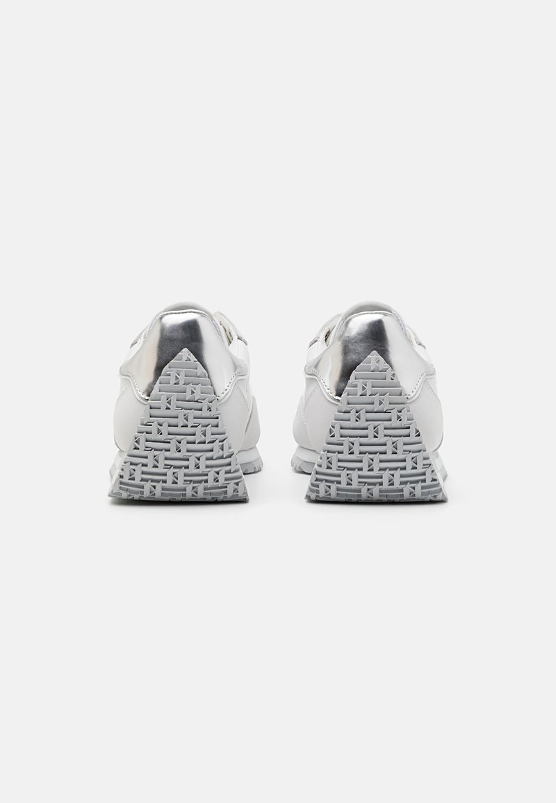 Zapatillas deportivas blancas con un upper de cuero suave, acentos en plata reflectante y suelas de goma gris con un patrón que incluye un diseño de tacón triangular.