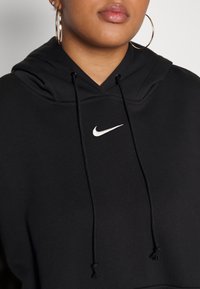 Čierna mikina s kapucňou vyrobená z mäkkej látky, s prednou kapsou, obsahujúca biele logo Nike a nastaviteľné šnúrky na kapucni.