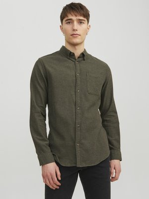 Camisa de botones verde oliva, tela texturizada, mangas largas, bolsillo en el pecho, dobladillo redondeado, botones marrones, combinada con jeans oscuros.