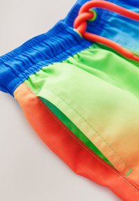Swim shorts featuring bright blue, green, orange, and gradient colors, with an elastic waistband and a colorful drawstring. Smooth fabric texture.