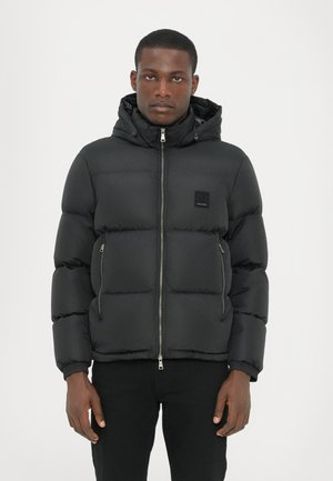 Black padded jacket with a zippered front, hood, and elastic cuffs. Features zippered side pockets and a small brand label on the chest.