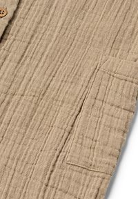 Beige textured fabric with a square pocket and a wooden button, featuring a wrinkled, quilted pattern.