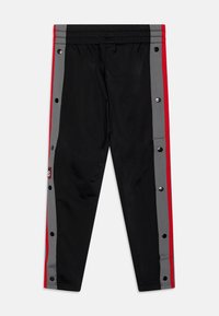 Schwarze Sporthose mit grauen Seitenpaneelen und roten Akzenten sowie Druckknöpfen. Das Material wirkt leicht und hat eine glatte Textur.