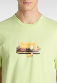 Lys grøn bomulds t-shirt med grafik af en gul plysbunny på en vintage vækkeur, der viser klokken 19:66 i røde cifre.
