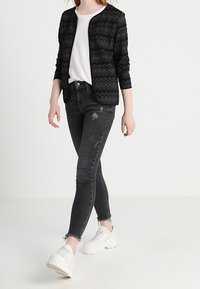 Černá bunda se zigzagovým vzorem přes bílé tričko, kombinována s roztrhanými černými skinny džíny a masivními bílými teniskami.