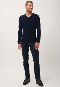 Navy-blauer V-Ausschnitt-Pullover aus weichem Material, kombiniert mit dunklen Jeans und schwarzen Schuhen; zeichnet sich durch ein tailliertes Design und gerippte Bündchen aus.