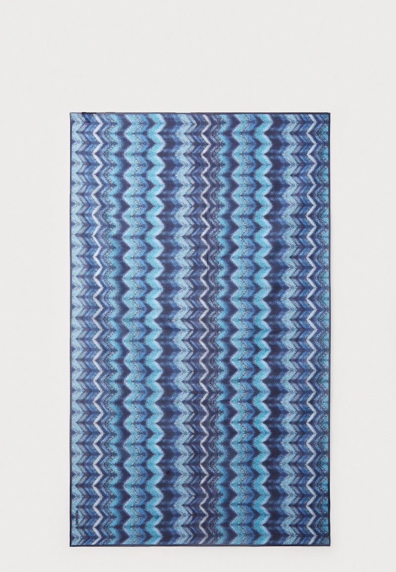 Rechthoekig tapijt met een zigzagpatroon in blauw en marineblauw, dat verschillende tinten mengt met een gestructureerd oppervlak. De randen zijn afgewerkt en schoon.