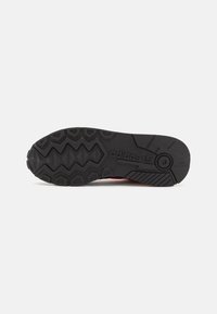 Podošva topánky Adidas s textúrovaným čiernym gumovým povrchom, s cik-cak vzormi a embosovaným logom pre lepšiu trakciu. Plochý, oválny tvar na päte.