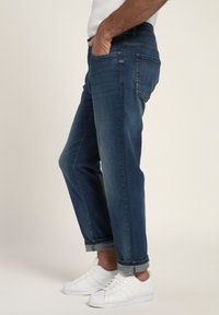 Jeans in denim blu scuro con una vestibilità comoda, dotati di orli risvoltati, tasche laterali e una leggera texture sbiadita. Abbinati a sneakers bianche.