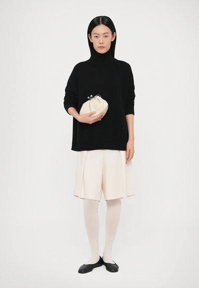 Pull noir à col roulé, coupe décontractée ; jupe plissée pale jusqu'aux genoux ; collants blancs ; ballerines noires ; tenant une pochette crème avec fermeture à clapet.