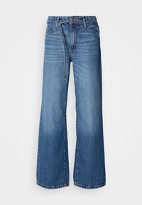Jean large bleu clair en denim. Présente une taille haute, des coutures visibles et une ceinture à nouer. Texture décolorée vers le bas.