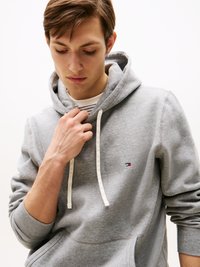 Hoodie cinza com cordão, apresentando um bolso frontal e um pequeno logotipo bordado. Textura suave com punhos e bainha canelados.