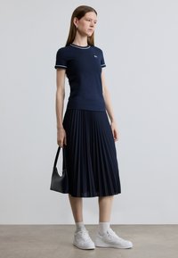 Μπλε ναυτικό μπλουζάκι με λευκή μπορντούρα, σετ με πλισέ μπλε ναυτικό φούστα. Η στολή περιλαμβάνει λευκά αθλητικά παπούτσια και μια μικρή μαύρη τσάντα.