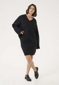 Abito in maglia nero con scollo a V, caratterizzato da un motivo a diamante testurizzato, maniche lunghe e una vestibilità rilassata. Indossato con scarpe platform nere.