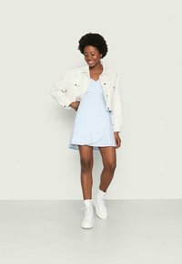 Vestido azul claro com um design envelope, mangas curtas, combinado com uma jaqueta de ganga branca. Botins brancos, tecido texturizado e padrão de bolinhas.