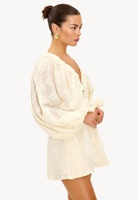 Vestido color crema con una tela suave y texturizada, con mangas abullonadas, un escote en V profundo y delicados patrones florales en toda la prenda.