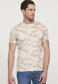 T-shirt à manches courtes en tissu léger. Présente un motif de feuilles beige et blanc. Design ajusté avec un col rond.