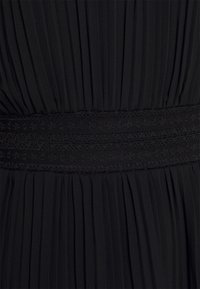 Tejido de vestido negro con plisados y una cinturilla de encaje negro texturizado. El material parece ligero y fluido, enfatizando su diseño elegante.