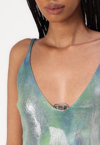 Särav ribaga tank top rohelise ja sinise gradientiga. Omab sügavat V-kaela ja hõbedast logo detaili kaeluses. Pehme tekstuur.