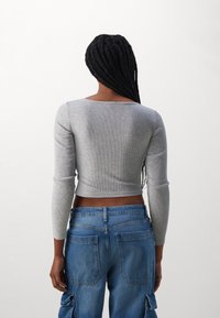 Top corto grigio a coste con maniche lunghe, caratterizzato da un collo a giro. Abbinato a jeans cargo blu con tasche posteriori e una vestibilità rilassata.