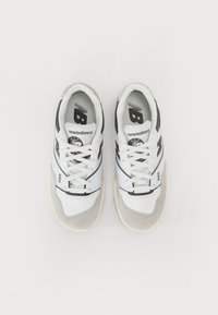 Tênis brancos e cinzas com um cabedal em couro texturizado e malha, detalhes em preto, atacadores proeminentes e marcação visível na língua e na lateral.