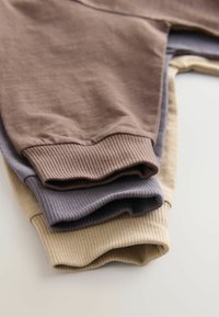 Drei Paare gerippte Baumwoll-Sweatpants in Braun, Grau und Beige, gestapelt, mit sichtbaren elastischen Taillenbündchen und Säumen.