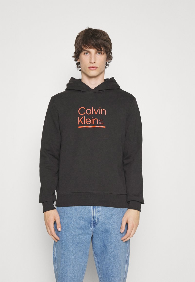 Black hoodie made of cotton with a kangaroo pocket. Features a red Calvin Klein logo and established date, ribbed cuffs, and hem.
