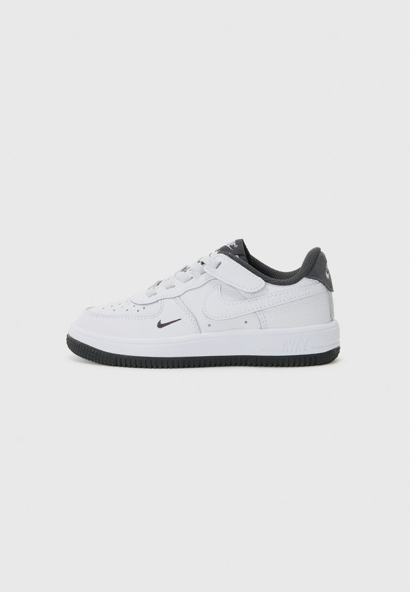 Nike Air Force 1-schoenen van wit leer met grijze accenten. Beschikt over een geperforeerde neus, vetersluiting en een zwarte rubberen zool.