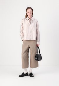 Stripet, lys rosa kortermet skjorte, beige culottbukser, svarte loafers, hvite sokker, bærer en liten svart håndveske. Enkelt design med rene linjer.