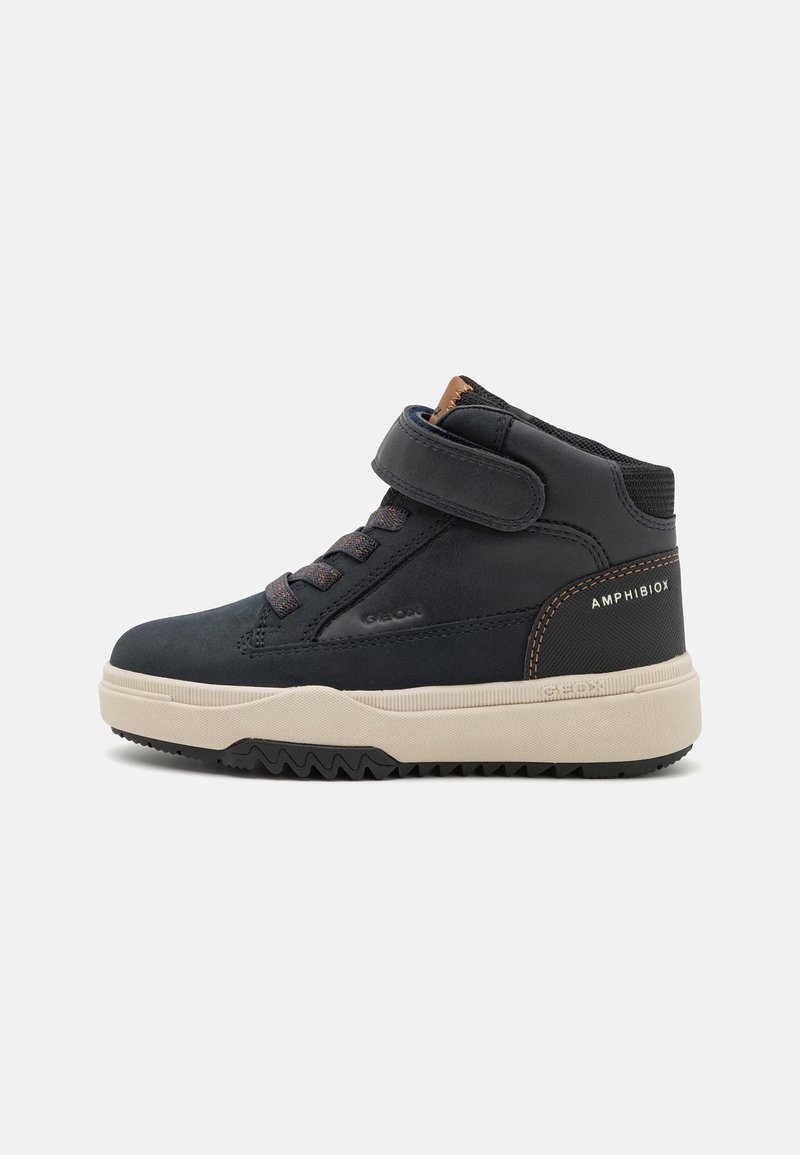 Chaussure montante noire avec une tige en daim et en maille, semelle en caoutchouc, sangle Velcro ajustable, et un intersole beige contrasté avec un motif en zigzag.