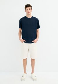 Camisa de manga corta de canalé en color navy con cuello redondo, combinada con pantalones cortos beige y zapatillas blancas, sobre un fondo claro y liso.