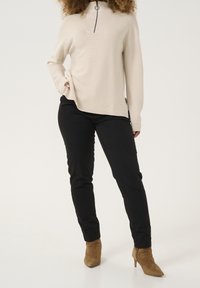 Beżowy sweter dzianinowy z kołnierzem na zamek, w połączeniu z czarnymi spodniami slim fit i brązowymi zamszowymi botkami za kostkę. Prosty design z delikatną fakturą.
