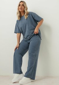 Blå oversized t-shirt och matchande vida byxor i mjukt tyg. Har subtil textur med sidostygn, i kombination med vita sneakers.