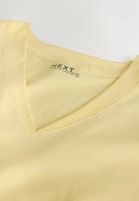 Geel V-hals T-shirt met korte mouwen van katoen, met "NEXT" merklabel en kleine maattekst binnen in de kraag.