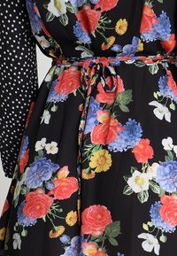 Vestido floral con fondo negro, que presenta rosas coloridas e hidrangeas azules. Mangas largas con lunares y un cinturón a juego.