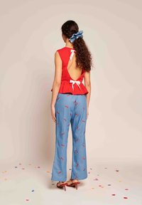Top peplum vermelho com recorte nas costas e laços brancos, combinado com calças largas azuis com padrão de cerejas. Modelo usa sandálias de salto vermelho.