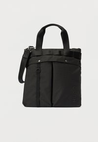 Svart stoff totebag med doble håndtak, frontlommer, avtakbar skulderreim og preget "HUGO"-logo nederst til høyre.