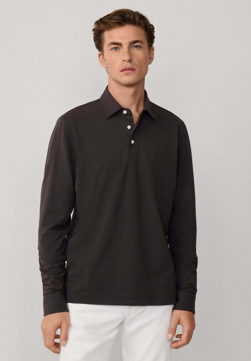 Polo a maniche lunghe marrone scuro con colletto classico, placca con tre bottoni e una texture morbida. Indossato con pantaloni di colore chiaro.
