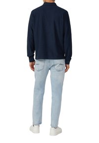 Marineblauer Strickpullover mit Kragen, kombiniert mit hellblauen Jeans. Der Pullover verfügt über gerippte Bündchen und eine lockere Passform. Weiße Sneakers runden den Look ab.